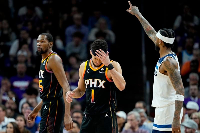 Phoenix Suns guard Devin Booker (1) rubs his forehead after a three pointer by Minnesota Timberwolves guard Nickeil Alexander-Walker, right, during the second half of Game 3 of an NBA basketball first-round playoff series, Friday, April 26, 2024, in Phoenix. (AP Photo/Matt York)