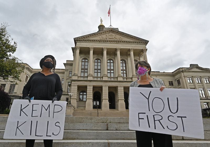 Activists hold signs on Thursday, April 30, 2020, as a processional led by hearses makes a stop at the state Capitol to illustrate what the demonstrators believe will be the deadly consequences of Gov. Brian Kemp’s rescinding of his sheltering-in-place order. (Hyosub Shin / Hyosub.Shin@ajc.com)