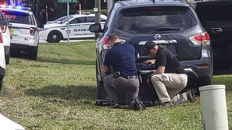 Law enforcement officials take cover outside a SunTrust Bank branch, Wednesday, Jan. 23, 2019, in Sebring, Fla. Authorities say they've arrested a man who fired shots inside the Florida bank. (The News Sun via AP)