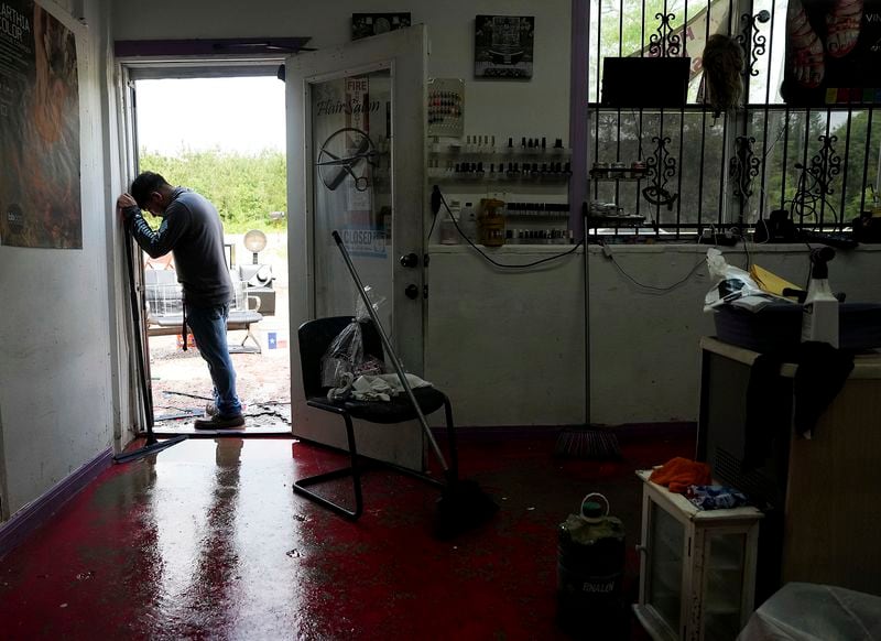 Cesar Villanueva stands in the doorway of his sister's salon, Arita's Hair Salon & Spa, while he tries to dry it out after days of heavy rainfall caused flooding in the area, Monday, May 6, 2024, in Plum Grove, Texas. (Elizabeth Conley/Houston Chronicle via AP)
