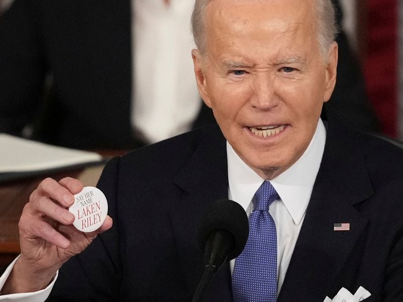 President Joe Biden holds up a button that says "Say Her Name Laken Riley." (AP Photo/Andrew Harnik)
