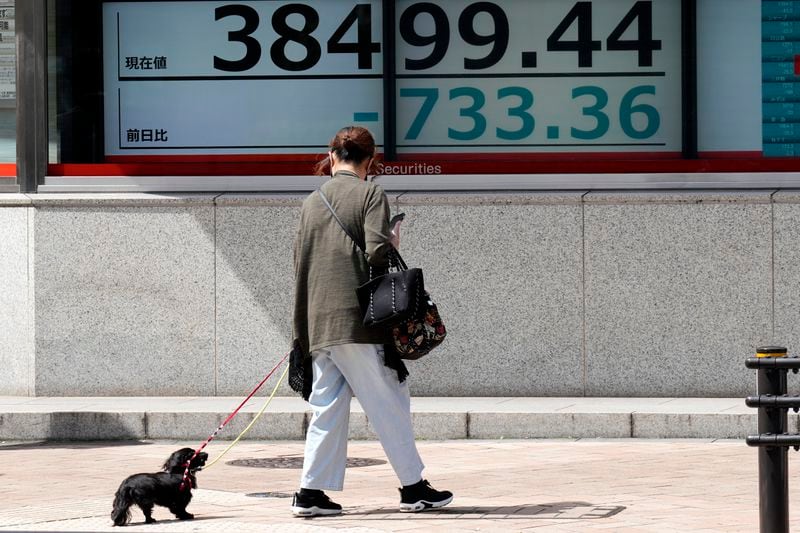 A person strolls with a dog in front of an electronic stock board showing Japan's Nikkei 225 index at a securities firm Tuesday, April 16, 2024, in Tokyo. (AP Photo/Eugene Hoshiko)