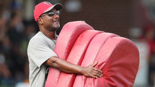 Falcons special teams coordinator Keith Armstrong carries some blocking pads out to the field for the first day of training camp on Thursday, July 28, 2016, in Flowery Branch.