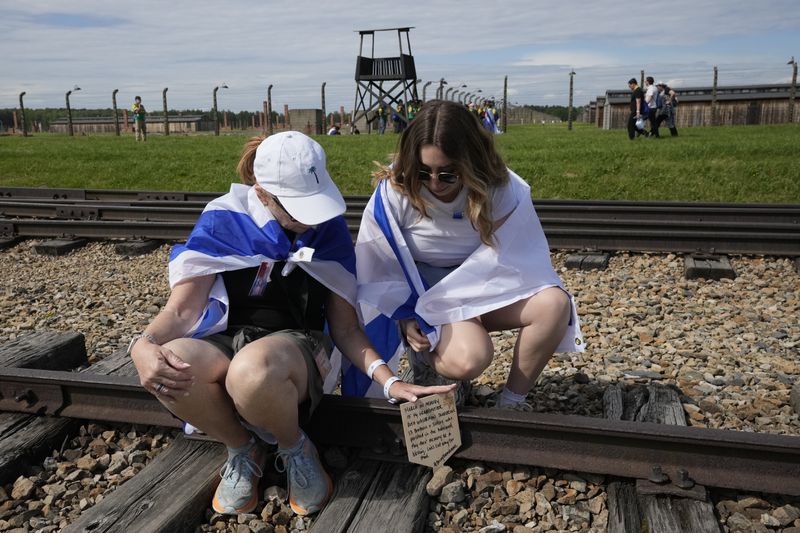 People sit on the train tracks at the former Nazi German death camp of Auschwitz-Birkenau as they attend the annual Holocaust remembrance event, the "March of the Living" in memory of the six million Holocaust victims in Oswiecim, Poland, Monday, May 6, 2024. The event comes amid the dramatic backdrop of the violence of the Israel-Hamas war after the Oct. 7 Hamas attack, the deadliest violence against Jews since the Holocaust, and as pro-Palestinian protests sweep U.S. campuses. (AP Photo/Czarek Sokolowski)