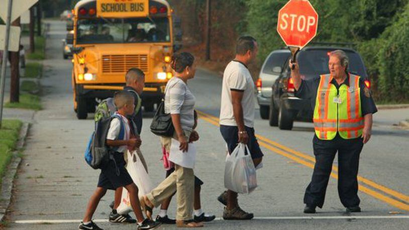 DeKalb, Atlanta and Gwinnett schools were among districts opening their doors to students on Monday. Faye Bishop, a 25-year DeKalb County police crossing guard, helps parents and children cross Curtis Drive near Woodward Elementary School.