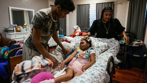 Tyrus Hike (left) helps his mother, Rhonda Jones, administer ibuprofen to Alayna at their home in Crown Point, Indiana. Alayna was injured during her birth and has cerebral palsy. She was recently hospitalized with respiratory syncytial virus, or RSV. (Taylor Glascock for KHN)