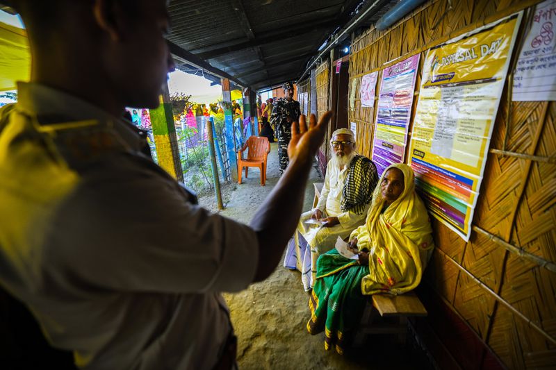 A police official instructs an elderly couple take rest sitting on a bench during the second round of voting in the six-week-long national election in Morigaon district, Assam, India, Friday, April 26, 2024. (AP Photo/Anupam Nath)