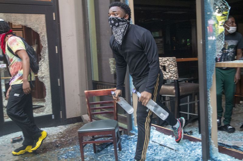 05/29/2020 - Atlanta, Georgia  - A protestor steals bottles of alcohol from McCormick & Schmick's Seafood Restaurant located in the CNN Center after a peaceful protest march turned into rioting and looting in Atlanta, Friday, May 29, 2020. (ALYSSA POINTER / ALYSSA.POINTER@AJC.COM)