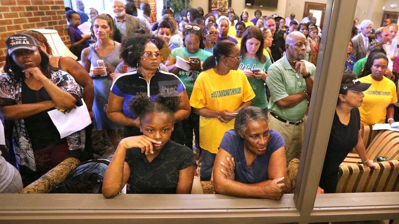 An overflow crowd watches from the lobby behind a glass window at the back of the room during the Buford Board of Education meeting on Monday, Aug. 27, 2018, in Buford. It was the first meeting since Superintendent Geye Hamby resigned amid allegations he used racial slurs to refer to black temporary construction workers and threatened violence against them. Curtis Compton/ccompton@ajc.com