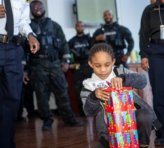 DeKalb County Sheriff’s Office holds the 16th annual Adopt-A-Family celebration on Tuesday, Dec 16, 2023 where Jamari Stell, 8, opens one of several gifts he is given at the party. Law enforcement officers donate their own money and buy gifts for about a dozen local children.  (Jenni Girtman for The Atlanta Journal-Constitution)