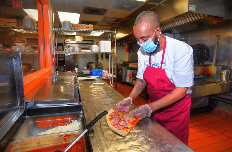 Edgewood Pizza owner Adonay Deglel, aka Bob Castanza (what everyone in the neighborhood calls him), prepares a couple of slices of his Hawaiian Delight Pizza in the kitchen of his Old Fourth Ward pizzeria in Atlanta. Pineapple on pizza is one of his least favorite toppings, but he offers it due to requests. CONTRIBUTED BY CHRIS HUNT PHOTOGRAPHY