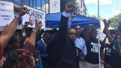 Deravis Thomas, center in blue suit, the father of Deravis Caine Rogers, raises his fist at a rally outside Fulton County courthouse Wednesday.
