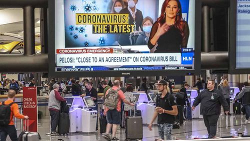 Travelers at Hartsfield-Jackson International Airport on Friday, March 13, 2020 as news coverage of the Coronavirus pandemic shows overhead. JOHN SPINK/JSPINK@AJC.COM