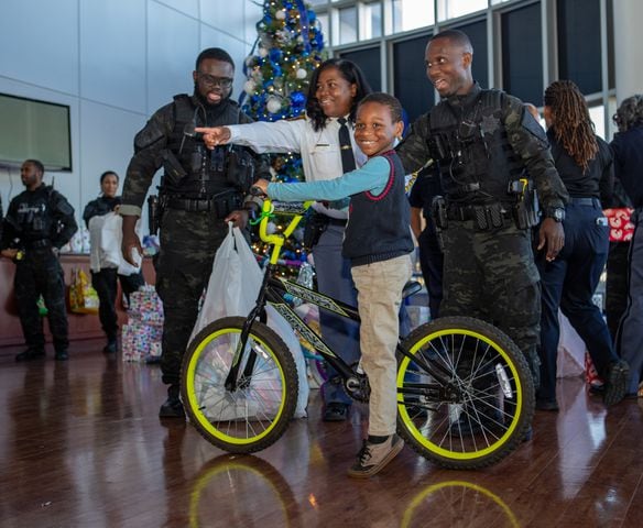 DeKalb County Sheriff’s Office holds the 16th annual Adopt-A-Family celebration on Tuesday, Dec 16, 2023 where Malachi Parks, 8, shows off his new bike at the party.  Law enforcement officers donate their own money and buy gifts for about a dozen local children.  (Jenni Girtman for The Atlanta Journal-Constitution)
