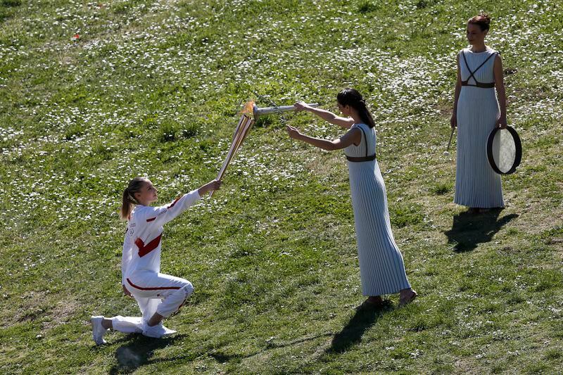 FILE - Greek actress Xanthi Georgiou, center, playing the role of the High Priestess, lights the torch of the 2020 Tokyo Olympic Games, held by Greek shooting Olympic champion Anna Korakaki, left, the first torchbearer, during the flame lighting ceremony at the closed Ancient Olympia site, birthplace of the ancient Olympics in southern Greece, March 12, 2020. On Tuesday, April 16, 2024 the flame for this summer's Paris Olympics will be lit and be carried through Greece for more than 5,000 kilometers (3,100 miles) before being handed over to French organizers at the Athens site of the first modern Olympics. (AP Photo/Yorgos Karahalis, File)