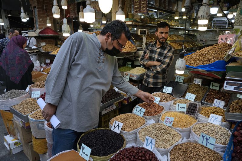 A potential customer inspects nuts at a shop at the old main bazaar in Tehran, Iran, Tuesday, April 16, 2024. Israel says it is poised to retaliate against Iran, risking further expanding the shadow war between the two foes into a direct conflict after an Iranian attack over the weekend sent hundreds of munitions into Israeli airspace. (AP Photo/Vahid Salemi)