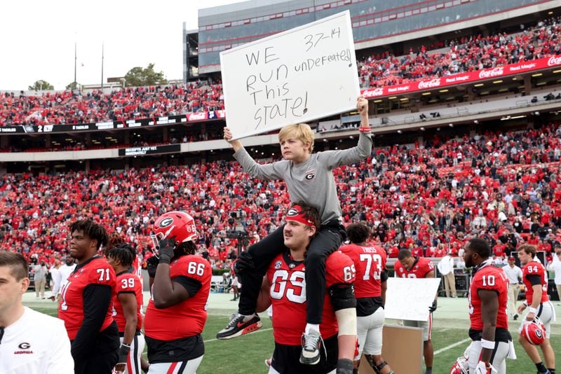 Georgia Bulldogs offensive lineman Tate Ratledge (69) gives Andrew Smart a ride on his shoulders as he holds a sign that reads, “We Run This State! 37-14 Undefeated!,” after Georgia’s 37-14 win against the Georgia Tech Yellow Jackets in a NCAA football game at Sanford Stadium, Saturday, November 26, 2022, in Athens, Ga. Andrew Smart is the son of Georgia Bulldogs head coach Kirby Smart. Jason Getz / Jason.Getz@ajc.com)