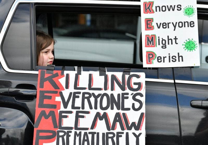 Maddie Nichols, 8, sits in the car as her mother Blythe Nichols (not pictured) decorates with signs before they participate in Drive-By protest against Gov. Brian Kemp's decision to re-open some Georgia businesses on Friday, April 24, 2020. (Hyosub Shin / Hyosub.Shin@ajc.com)