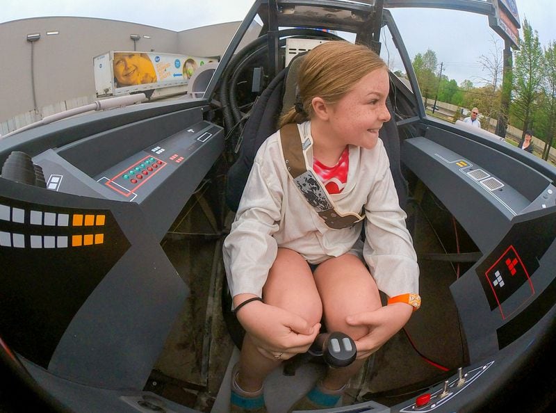Reese Hagler, 8, sits in the cockpit of the near life-like replica of an X-Wing Starfighter from Star Wars at Embry Village shopping center in Embry Hills on Saturday, April 16, 2022. (Steve Schaefer / steve.schaefer@ajc.com)