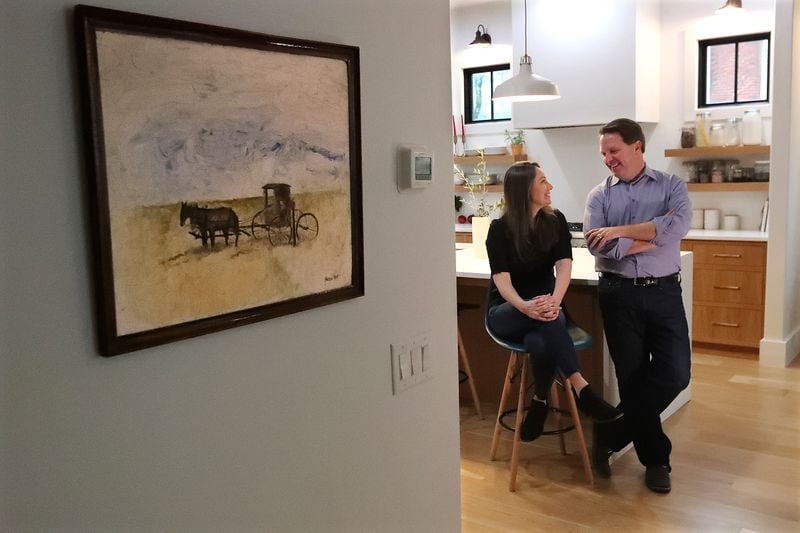 A 1969 oil painting by his father Ed Paxton is one of the few wall hangings in the home of Matt Paxton and minimalist expert Zoe Kim, seen here relaxing in their kitchen in Suwanee. Curtis Compton / Curtis.Compton@ajc.com