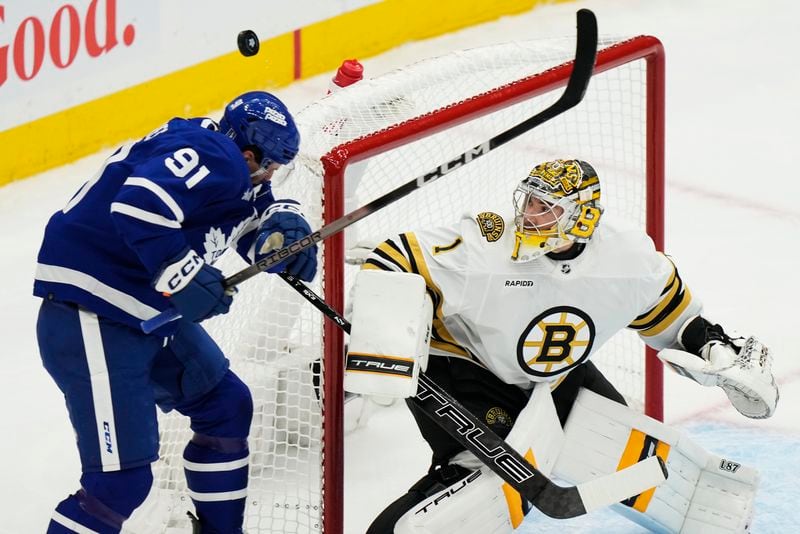Toronto Maple Leafs' John Tavares (91) is hit by the puck as Boston Bruins goaltender Jeremy Swayman (1) watches during the first period on Game 3 of an NHL hockey Stanley Cup first-round playoff series in Toronto on Wednesday, April 24, 2024. (Frank Gunn/The Canadian Press via AP)