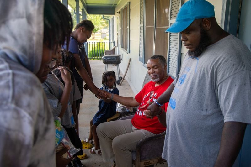Charlie Thomas (center, in red) is prayed for by Mauriceo Martin (blue hat) and other volunteers with the Malachi Project as they serve neighbors in the McDonough Housing Authority Complex. PHIL SKINNER/ FOR THE AJC