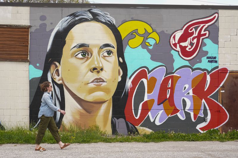 A pedestrian walks past a mural by Kwazar Martin featuring Indiana Fever player Caitlin Clark on the near west side of Indianapolis, Tuesday, April 16, 2024. The Fever selected Clark as the No. 1 overall pick in the WNBA basketball draft. (AP Photo/Michael Conroy)