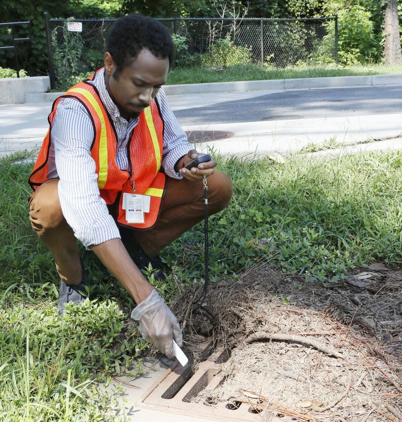 Matthew Calhoun, an environmental health inspector from the DeKalb County Health Department’s Division of Environmental Health, drops a larvicide briquette into one of the storm drains at Brookside Park to help control mosquitoes. BOB ANDRES / BANDRES@AJC.COM