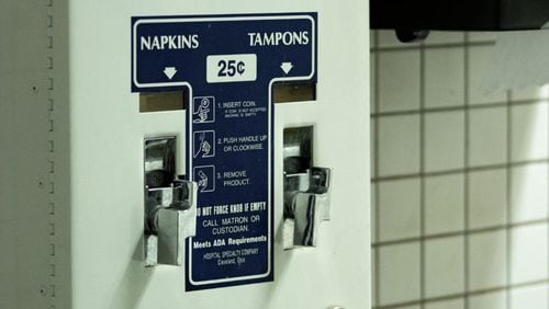 feminine hygiene product dispenser in bathroom with blue labels saying pad and tampon for 25 cents