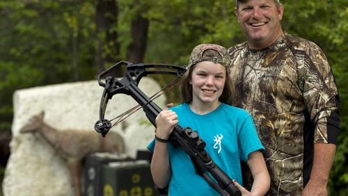 Stormy Smith with her dad, Todd, and her crossbow. Smith took Stormy his Bartow County hunting camp when she was 10 and was surprised that she became interested in hunting herself. Last year, at 11, she shot and killed her first doe with a crossbow. She's now 12 and is hoping to shoot a buck this fall. Ben Gray / bgray@ajc.com