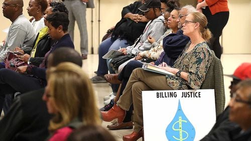 Joyce Christman of Druid Hills, with her sign, is looking for billing justice along with dozens of other DeKalb County residents demanding answers for excessively high water bills during a town hall meeting at the Maloof Auditorium in Decatur on Thursday. Curtis Compton/ccompton@ajc.com