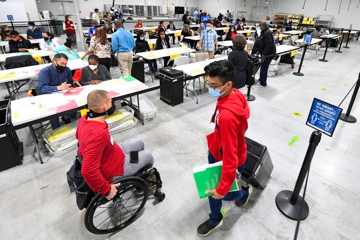 An election worker pulls a case full of ballots past an observer in a wheelchairas as votes for President are recounted at the Gwinnett County elections office on Friday, Nov.13, 2020 in Lawrenceville. (JOHN AMIS FOR THE ATLANTA JOURNAL-CONSTITUTION)