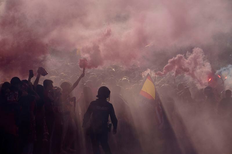 Police officers stand guard as supporters burn flares outside the Metropolitano stadium, ahead of the Champions League quarterfinal first leg soccer match between Atletico de Madrid and Dortmund in Madrid, Spain, Wednesday, April 10, 2024. This week's Champions League soccer games will go ahead as scheduled despite an Islamic State terror threat. A media outlet linked to the terror group has issued multiple posts calling for attacks at the stadiums hosting quarterfinal matches in Paris, Madrid and London. (AP Photo/Andrea Comas)