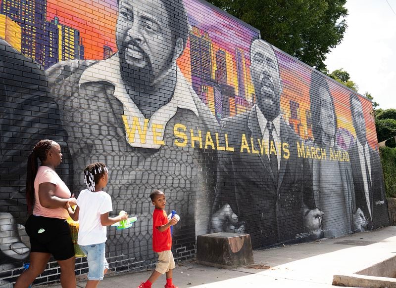 July 13, 2020, Atlanta — A family walks pass a mural on the side of Privado Barbershop in Vine City. The owner, Samuel Glickman, opened his shop up for “The Confess Project,” an organization that enlists barbershops like Privado to double as mental health centers, where Black men can comfortably talk about their issues. (RYON HORNE/RHORNE@AJC.COM)
