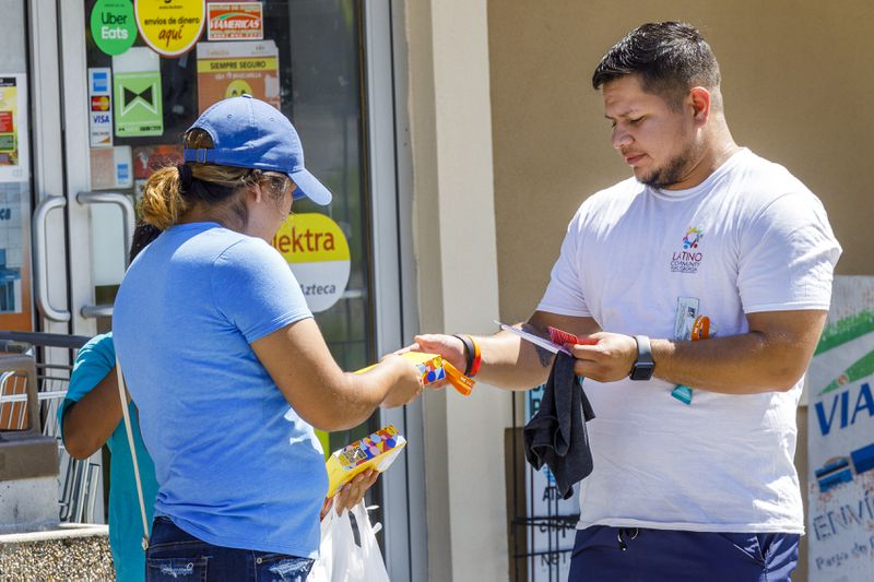 Lani Gutierrez, a navigator with Latino Community Fund Georgia, right, distributes COVID-19 test kits, and cloth neck gaiters for sun protection during a community outreach event held outside a store Saturday in Valdosta, Ga. The organization does a lot of outreach to farm workers about how to report abusive conditions. Colin Hackley  for The Atlanta Journal-Constitution
