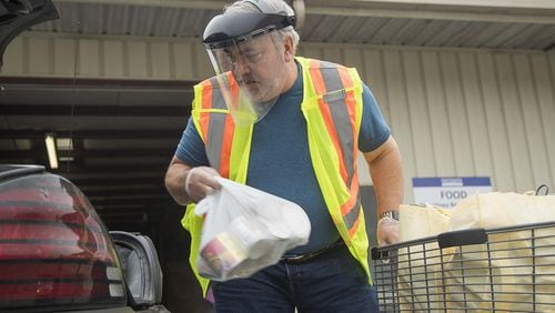Sweetwater Mission executive director Brian Hamilton places pre-bagged groceries inside a patron’s vehicle during food distribution “drive-through” at the Austell facility. Hamilton, along with other volunteers and employees, wore protective wear while facilitating the food distribution. Normally patrons are allowed inside the facility to pick out their own food but operations have shifted due to coronavirus. ALYSSA POINTER/ALYSSA.POINTER@AJC.COM