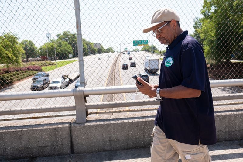 Darryl Haddock, the director environmental education for the West Atlanta Watershed Alliance, walks over I-20 in the West End holding a device that transmits temperature data to his phone to map the air temperature as he walks Wednesday, June 15, 2022, as part of a research study. (Ben Gray for the Atlanta Journal-Constitution)