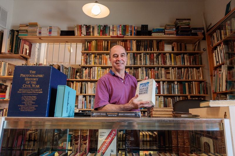 Frank Reiss, owner of A Capella Books in Atlanta, poses for a portrait with a signed copy of David Foster Wallace’s "Infinite Jest" on Friday, Aug. 5, 2022. (Arvin Temkar / arvin.temkar@ajc.com)
