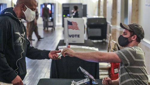 C.J. Andrews (right) checks in voters at Park Tavern located at 500 10th Street NE in Atlanta on Tuesday, Nov. 2, 2021.  (John Spink / John.Spink@ajc.com)