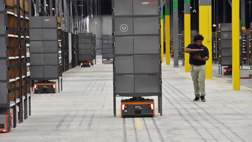 Isaac Jones of Project Verte monitors a warehouse robot in a training run as it moves a shelving unit to a station where a worker will remove ordered items. Robotics and artificial intelligence are quickly changing the warehouse business and jobs. Robots help the human get more done in shorter amounts of time. The upside is workers handle orders faster. The downside is fewer people are needed to get the work done than in less-automated warehouses. HYOSUB SHIN / HSHIN@AJC.COM