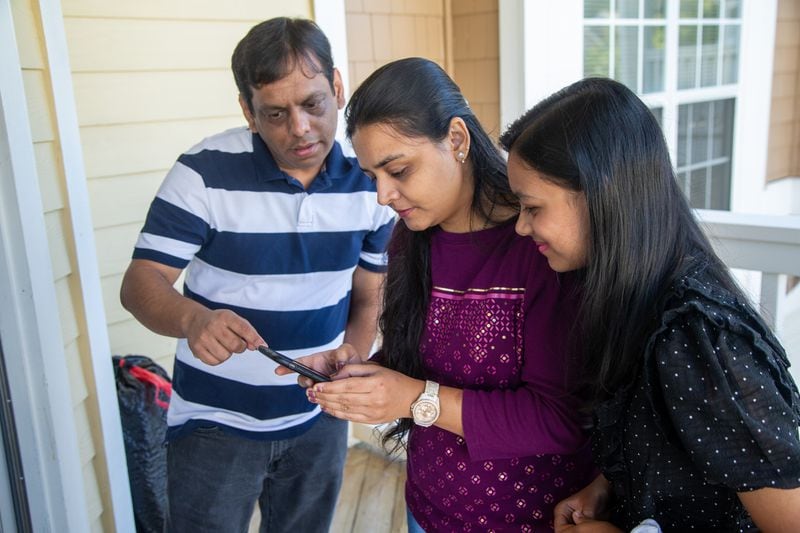 Mehul Bhatt (from left), his wife Hita and daughter Aesha work together on a phone in their home. 
PHIL SKINNER FOR THE ATLANTA JOURNAL-CONSTITUTION.
