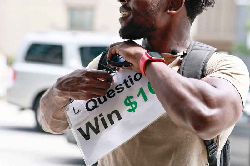 TikTok star Leon Ondieki pins a sign to his backpack before starting his trivia game on Friday, July 22, 2022. (Natrice Miller/natrice.miller@ajc.com)