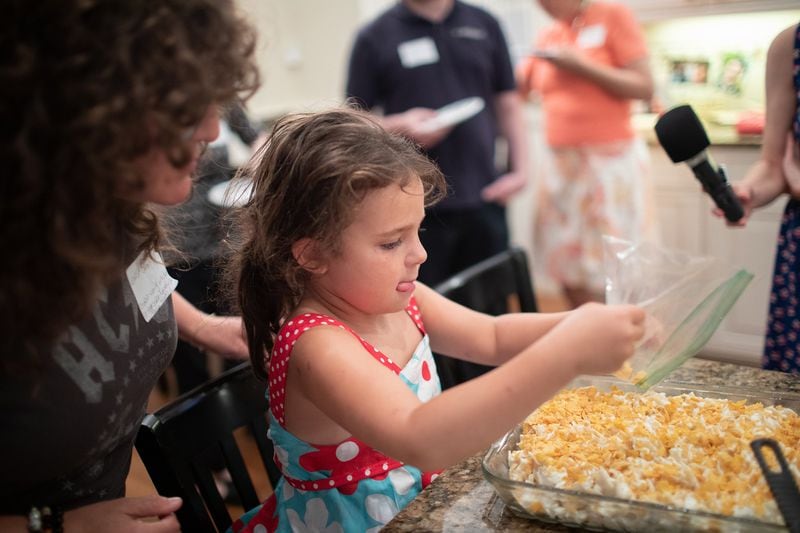 Five-year-old Alice Simmons puts the final touch on the kugel, sprinkling the top with lightly crushed corn flakes. CONTRIBUTED BY EUGENE BUCHKO