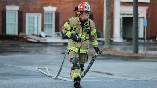 Firefighters mop up after a predawn fire destroyed a medical office building in Alpharetta. The city is seeking a federal grant to buy specialized washing machines to handle firefighters’ turnout gear. JOHN SPINK / JSPINK@AJC.COM