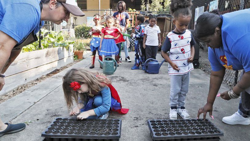 Germaine Appel (left), the school’s garden educator, and teacher Danielle Brown help kids plant seeds in the school garden on Sept. 11, 2019. Little Ones Learning Center in Forest Park is one of 18 state farm to school demonstration projects: Students grow and harvest food, and the school sells it to their parents and to the surrounding neighborhood. BOB ANDRES / ROBERT.ANDRES@AJC.COM