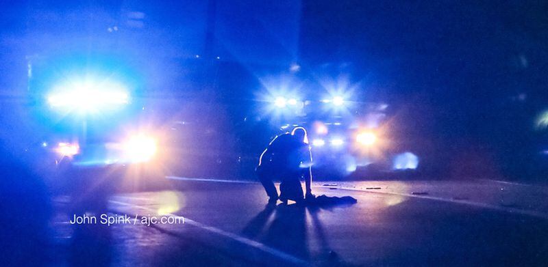 A DeKalb County police officer examines clothing in the middle of I-85 North near the North Druid Hills Road exit. JOHN SPINK / JSPINK@AJC.COM