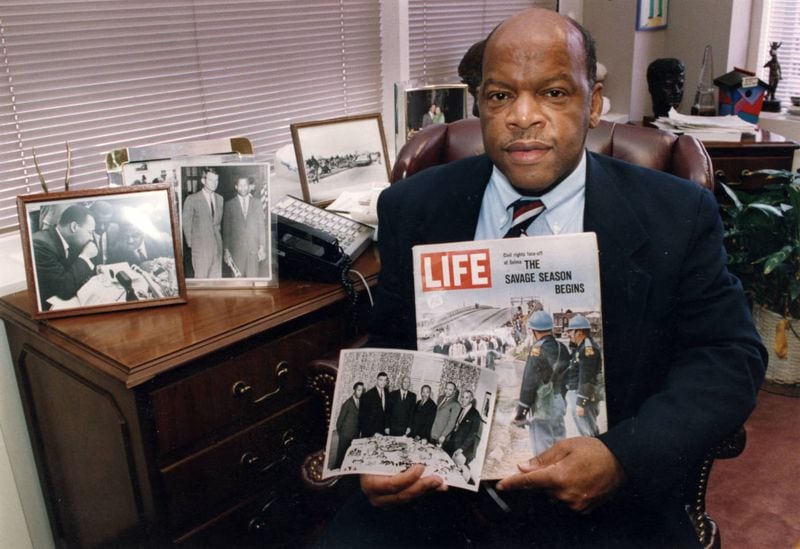 Congressman John Lewis in his Atlanta office  on Jan. 20, 1994, with two of his favorite items from his collection of memorabilia from his younger days as a civil rights activist in the 1960s. He is holding a Life Magazine cover picturing the famous Selma march in 1965. (He is in this photo at front of the line of marchers.) He is also holding a photo of the 'Big Six' civil rights leaders of the time to plan for the famous March on Washington. The men in the photo are L to R: John Lewis, Whitney Young, A. Phillip Randolph, Martin Luther King, James Farmer, and Roy Wilkins. In background photos (picture at left) of Dr. Martin Luther King with Fred Shuttlesworth and Ralph Abernathy and Lewis with Robert Kennedy (picture at right). (Kimberly Smith / AJC Archive at GSU Library AJCP452-146f)
