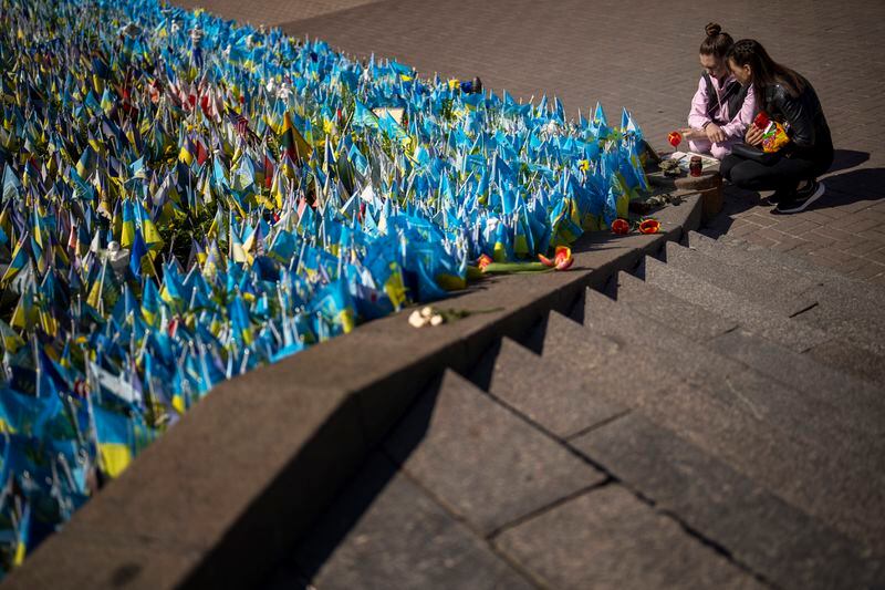Two woman look at Ukrainian flags placed in memory of civilians and soldiers killed during the war at the Independence square in central Kyiv, Saturday, April 20, 2024. (AP Photo/Francisco Seco)