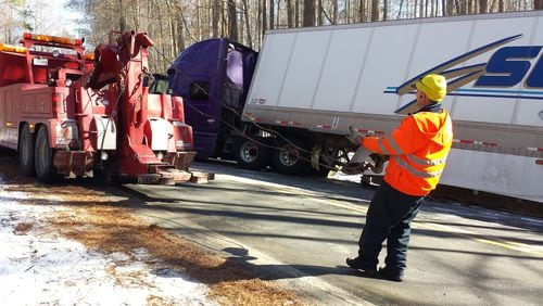 A tow truck pulls an 18-wheeler out of a ditch in south Fulton County on Thursday.