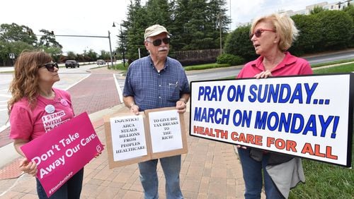 Protesters, from left, Anita Tucker, Michael Blundell and June Krise display signs opposing the new Senate health care repeal bill outside U.S. Sen. Johnny Isakson’s office on Friday. HYOSUB SHIN / HSHIN@AJC.COM